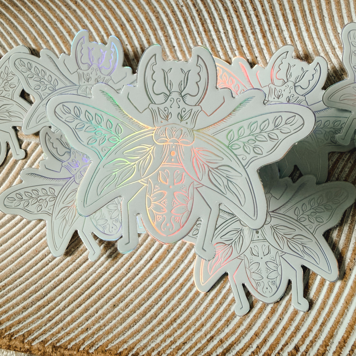 a holographic beetle sticker that is adorned with flowers and leaves and is hovering above several others that are resting on a striped dish.