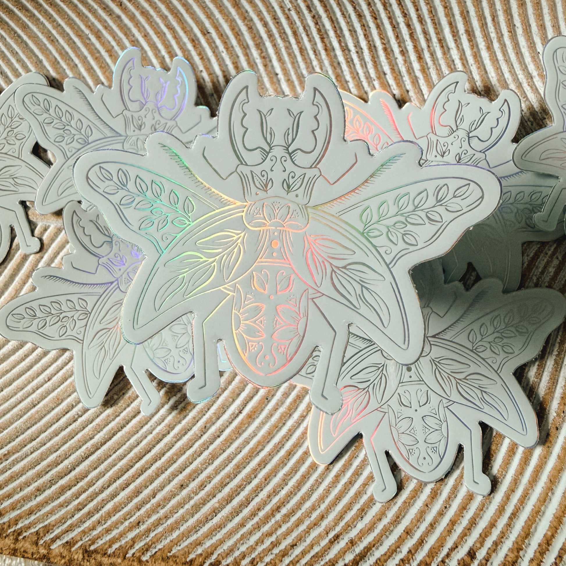 a holographic beetle sticker that is adorned with flowers and leaves and is hovering above several others that are resting on a striped dish.
